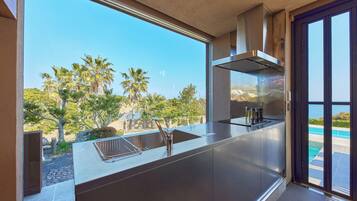 A modern kitchen with a stainless steel island, a built-in oven, and a view of a pool and palm trees.