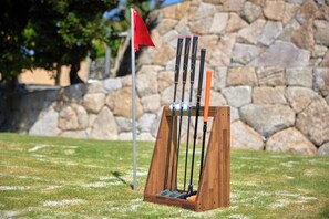 A golf club set on a wooden stand with a stone wall and flag in the background.