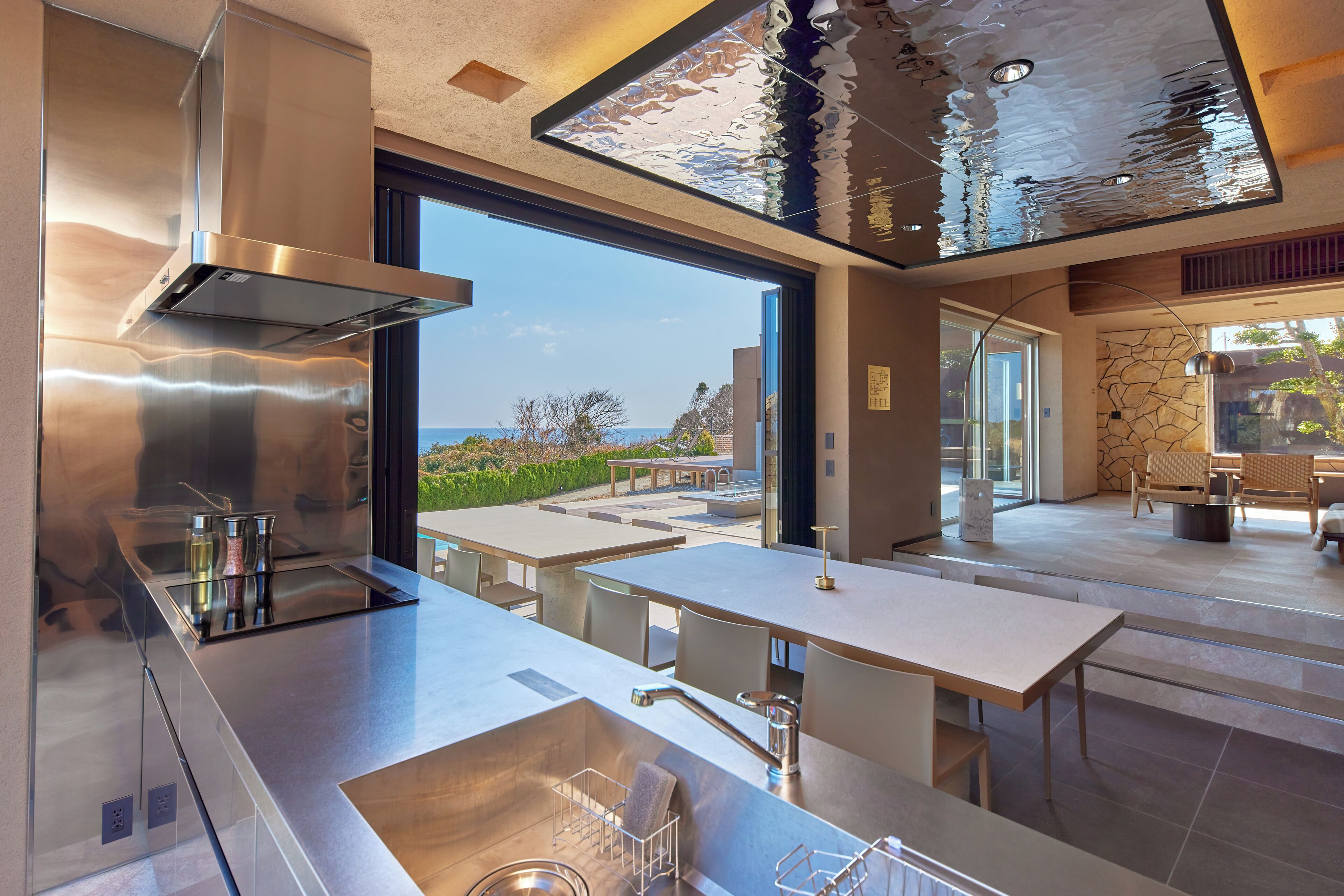 A modern kitchen with a large window, stainless steel appliances, and a dining area with outdoor seating.