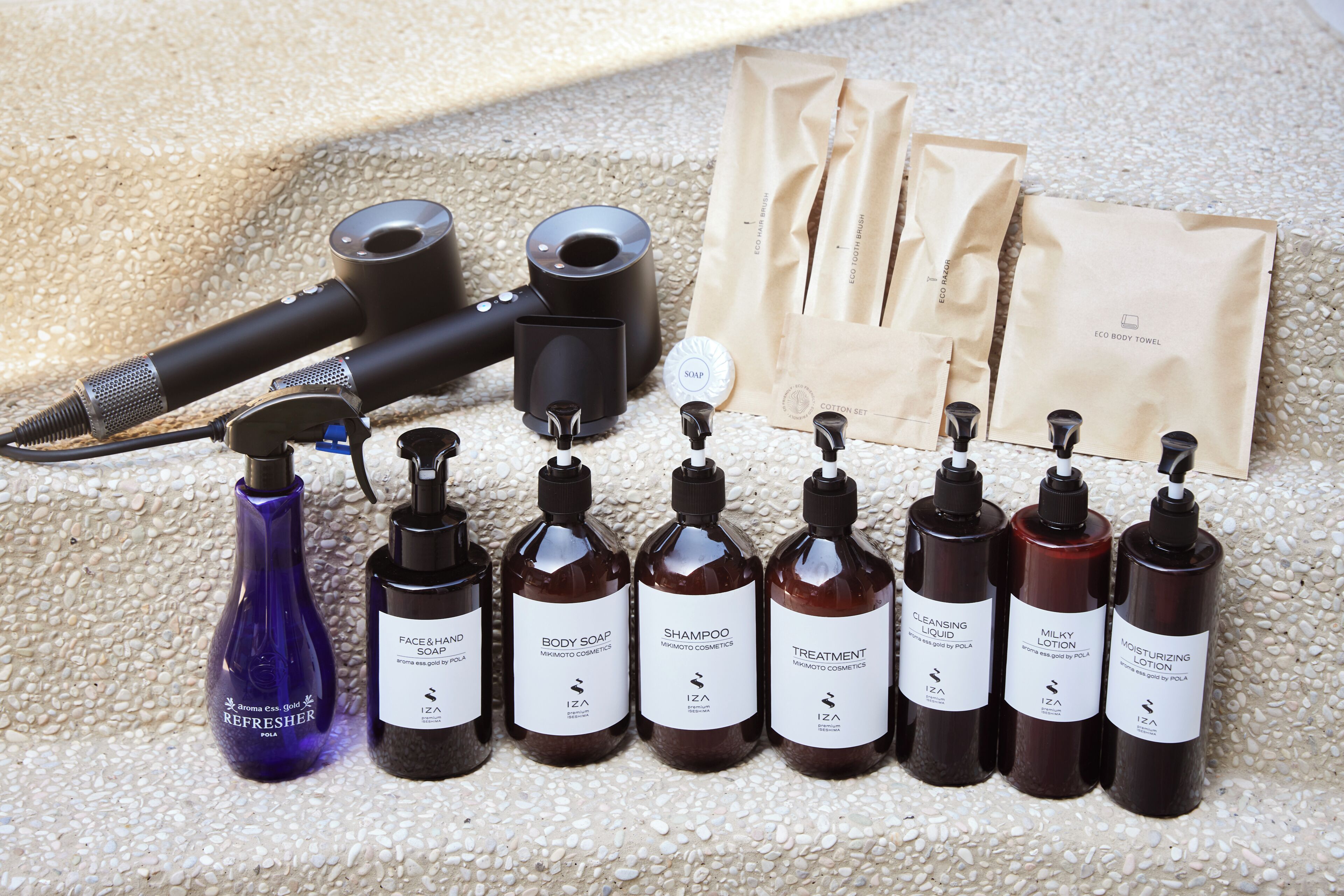 Diverse verzorgingsproducten, waaronder flessen douchegel, shampoo en bodylotion, samen met een haardroger en een set katoenen handdoeken.