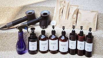 Diverse verzorgingsproducten, waaronder flessen douchegel, shampoo en bodylotion, samen met een haardroger en een set katoenen handdoeken.