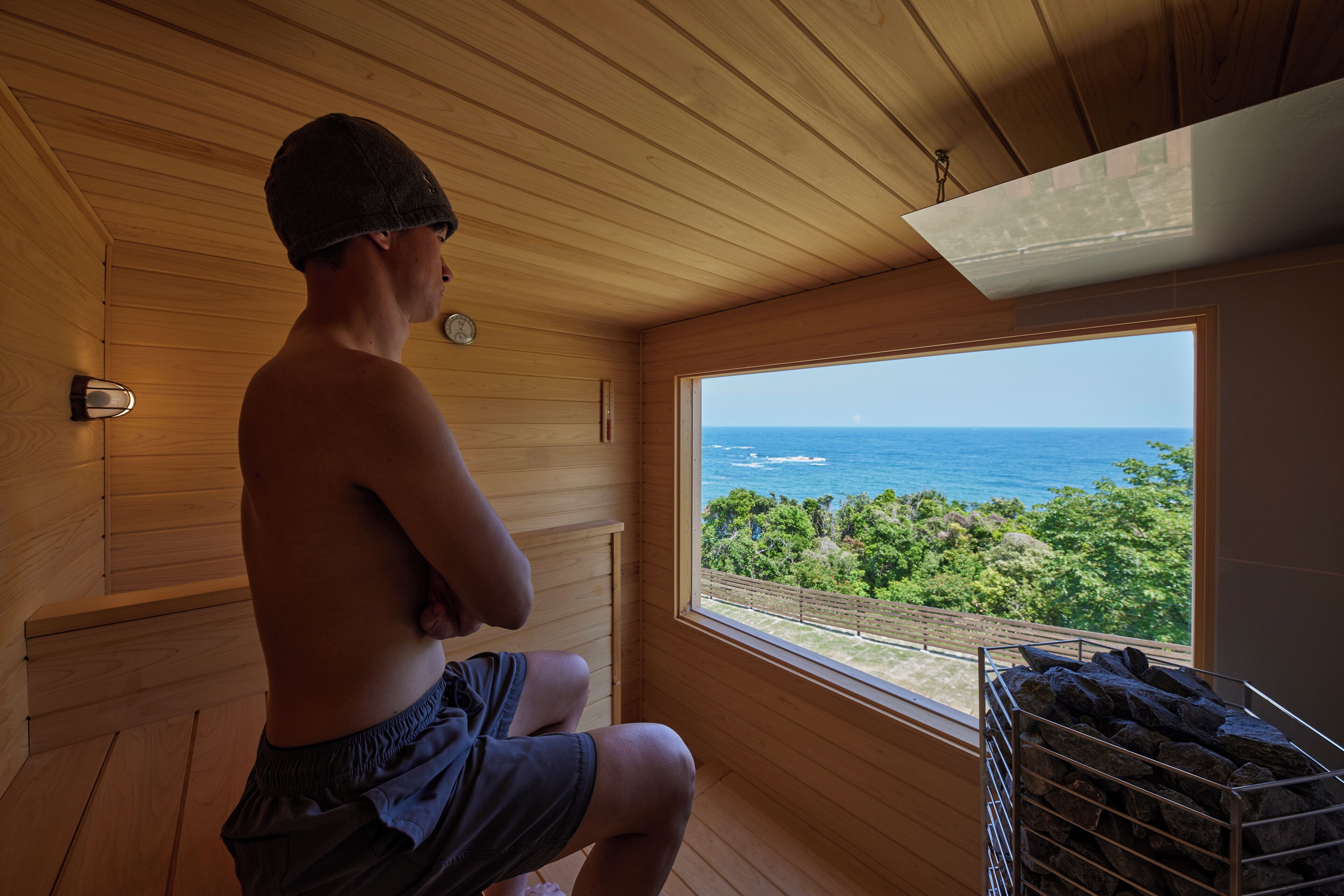 A person seated in a wooden cabin with a view of the ocean through a window.