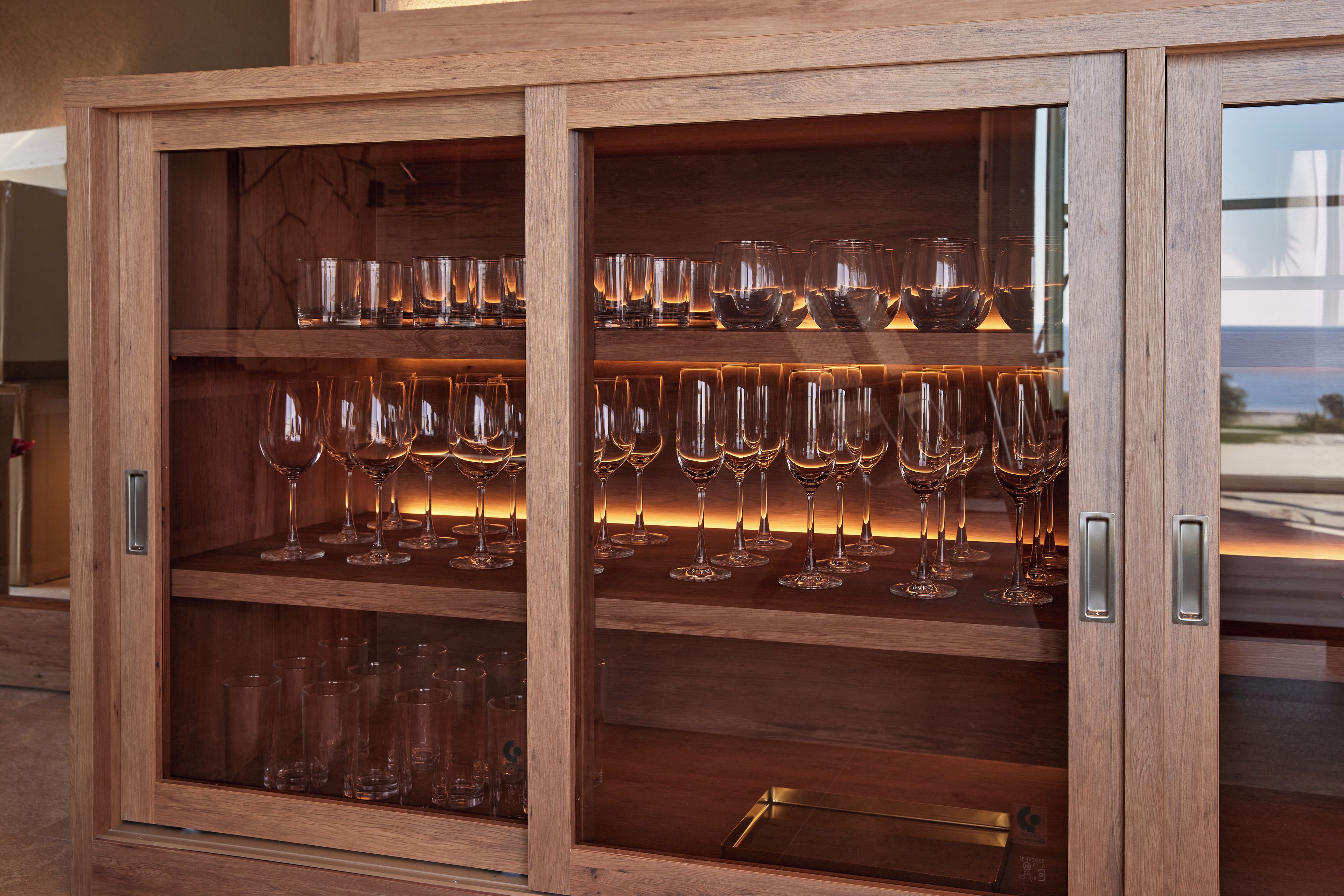 A wooden cabinet with multiple shelves containing wine glasses and tumblers.