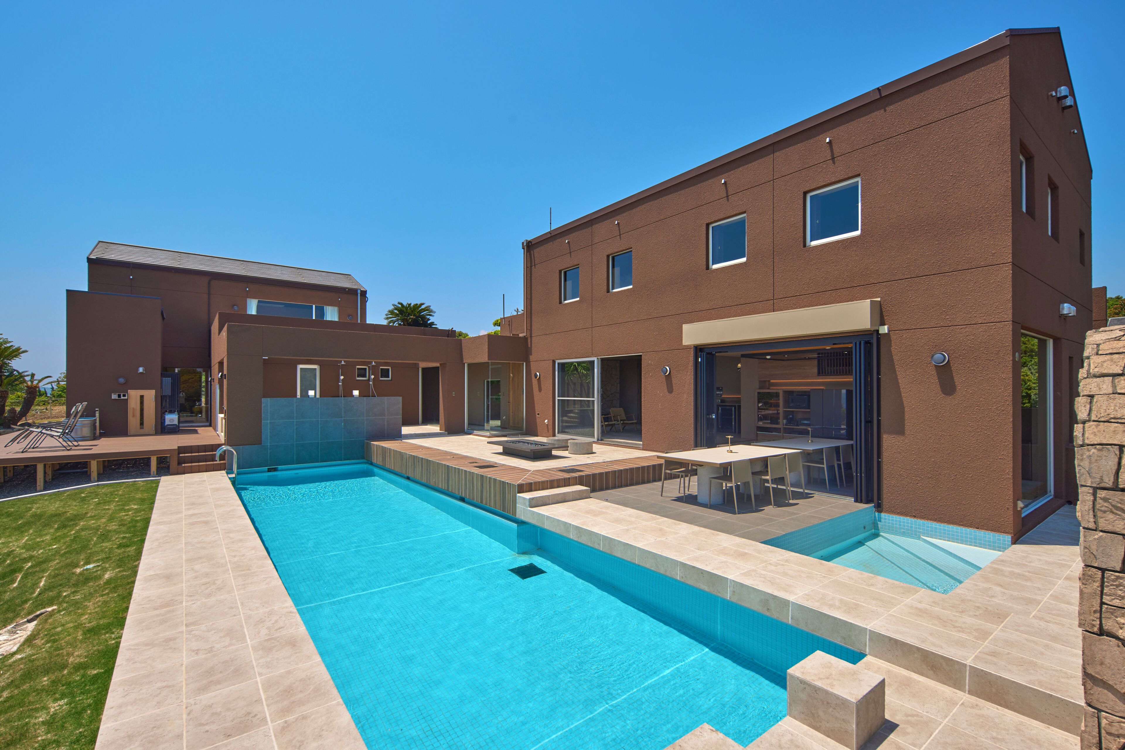 Et moderne hus med to etager, en swimmingpool, udendørs møbler og en patio.