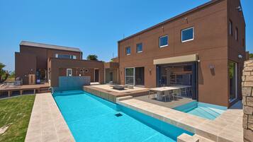 Et moderne hus med to etager, en swimmingpool, udendørs møbler og en patio.