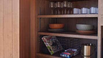 Un estante de madera con platos, tazones y un recipiente metálico apilados.