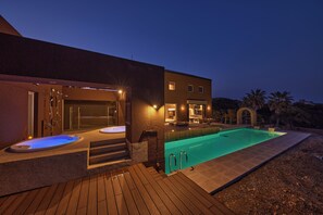 Una casa moderna con piscina, jacuzzis exteriores y un patio bien iluminado.