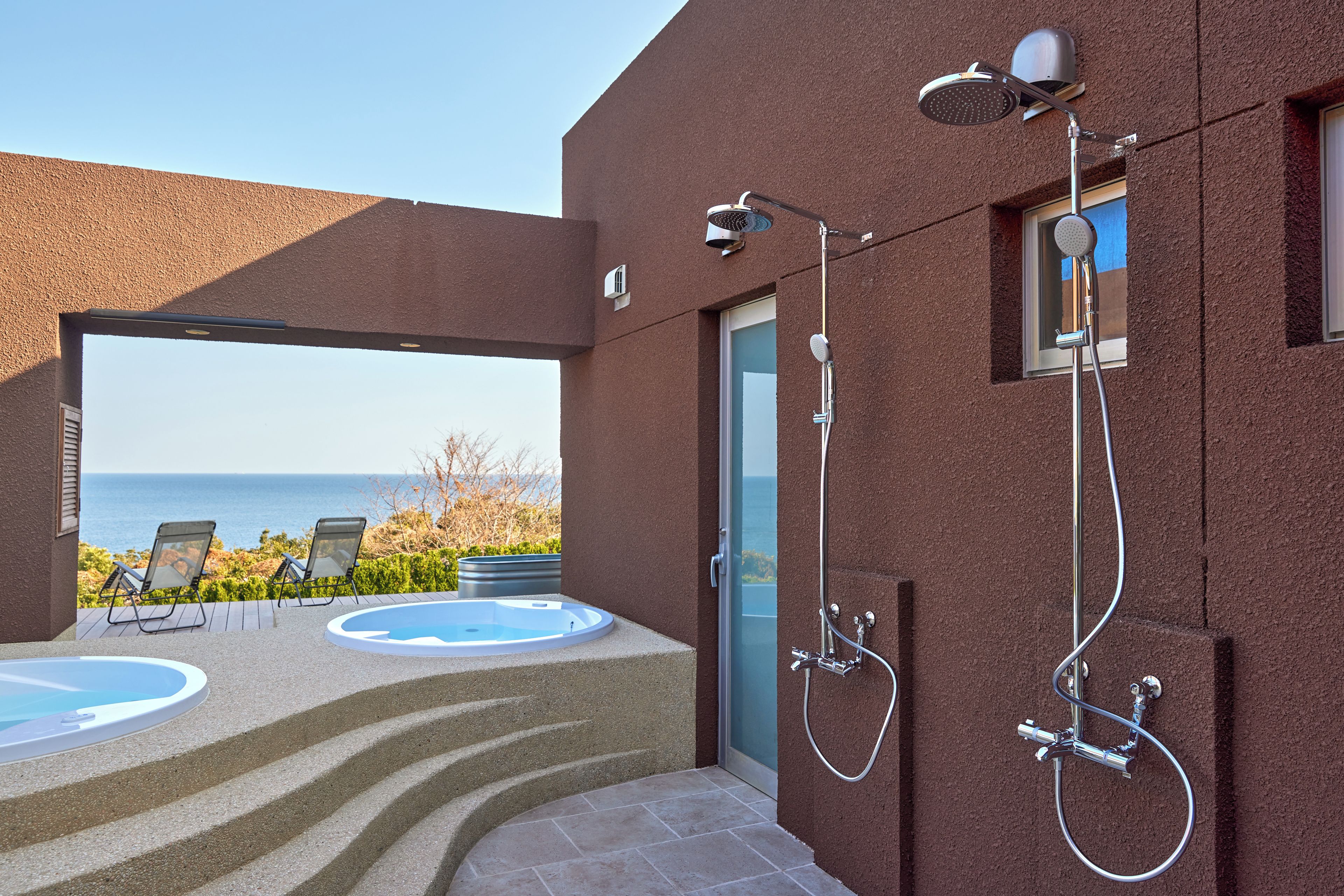 Ein moderner Poolbereich im Freien mit Whirlpool, Dusche und Meerblick.