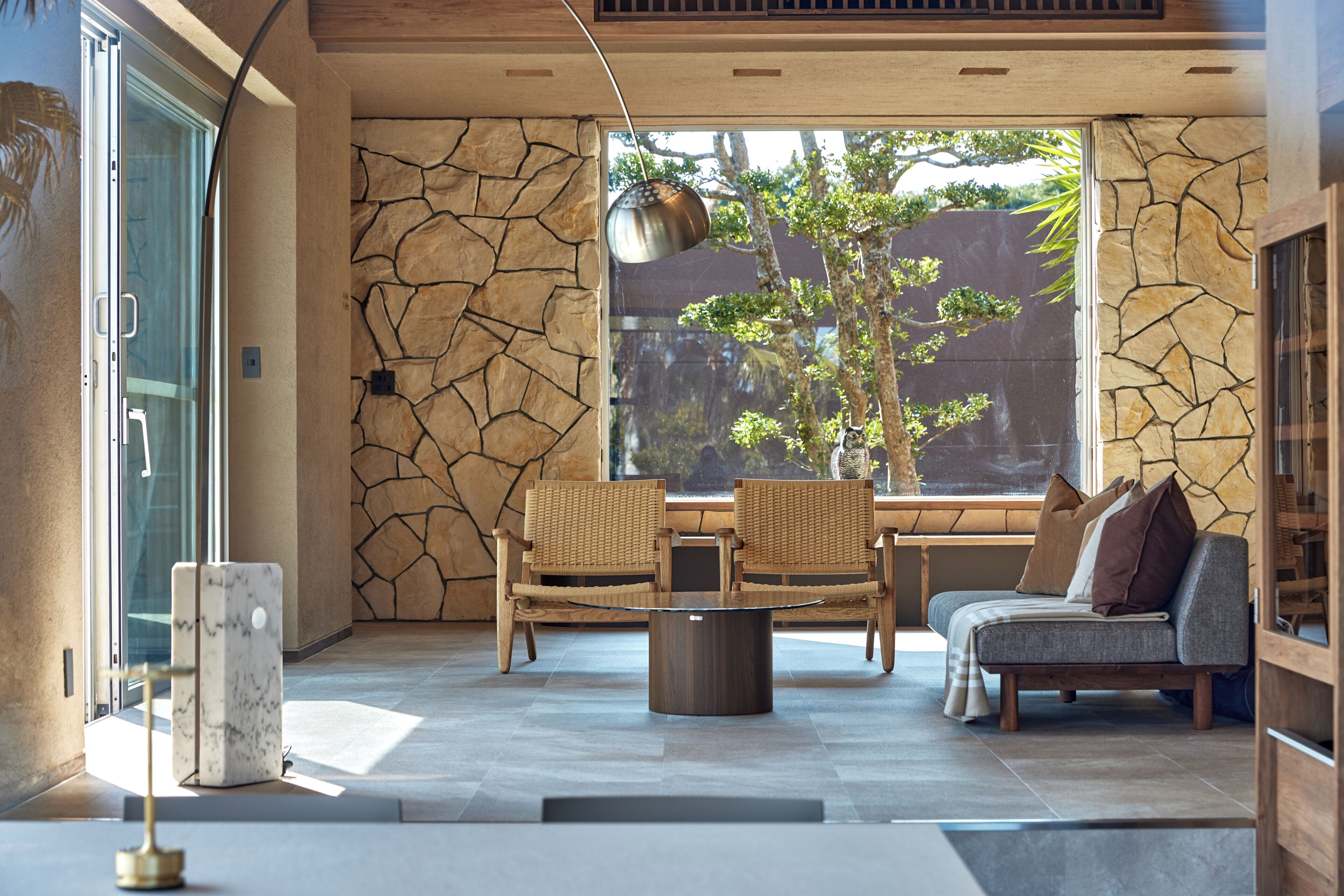 Un intérieur moderne avec des murs en pierre, un coin repas avec des chaises, un canapé et une grande fenêtre donnant sur la forêt.