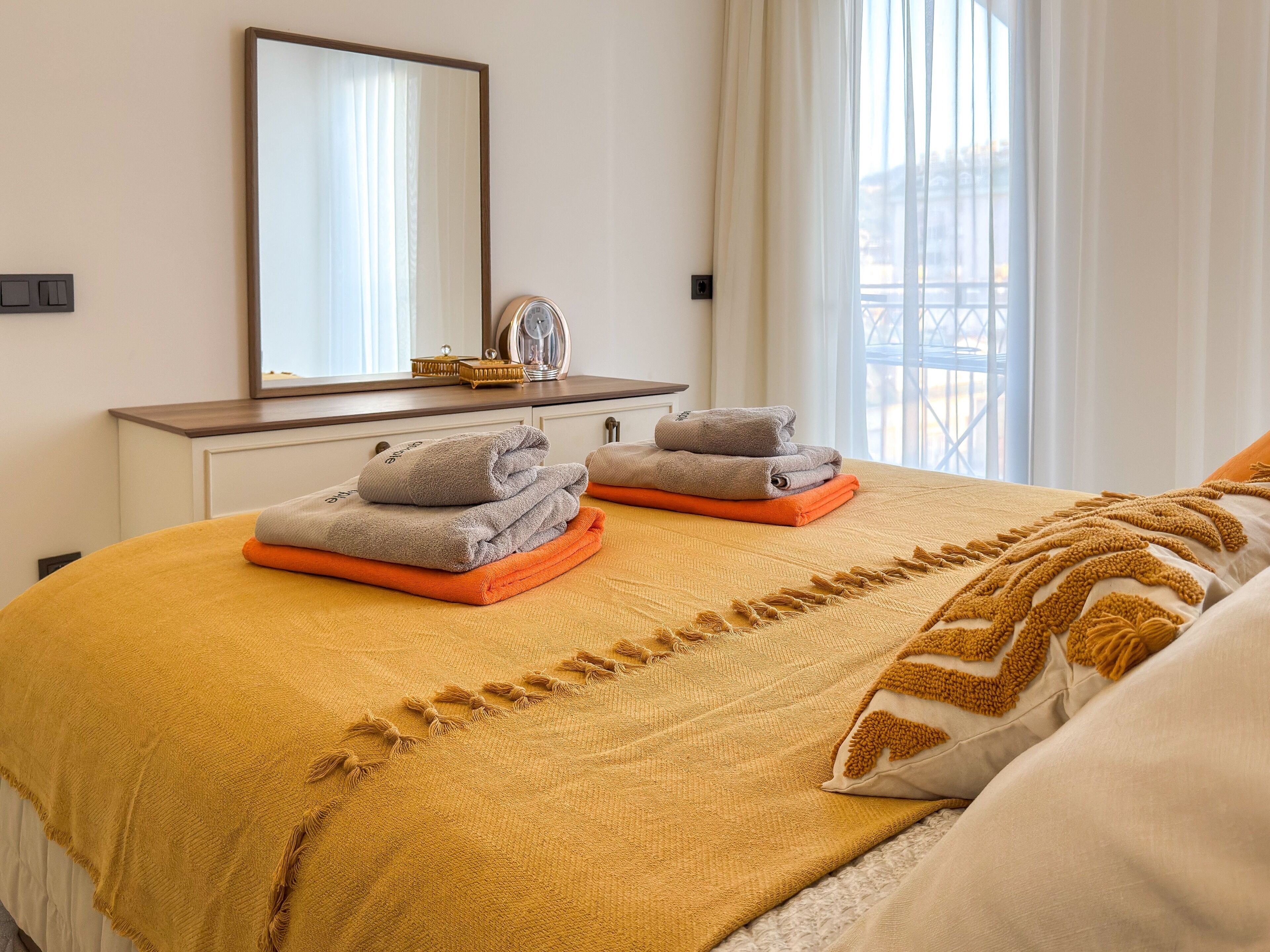 A hotel room with a bed, a bedside table, a mirror, and a window with curtains.