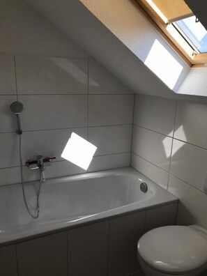 A bathroom with a skylight, a bathtub, and a toilet. - Wohnen am Wanderweg II (Aurich)