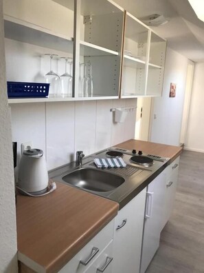 A compact kitchen with a sink, stove, and cabinets, and a mirrored backsplash. - Wohnen am Wanderweg II (Aurich)
