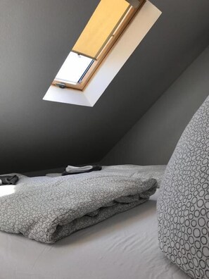 A room with a sloped ceiling, a skylight, a bed with a patterned blanket, and a pillow with a geometric design. - Wohnen am Wanderweg II (Aurich)