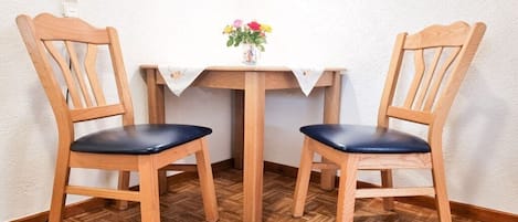 Dos sillas de madera con cojines negros, una mesita de madera con mantel blanco y un jarrón con flores sobre la mesa.
