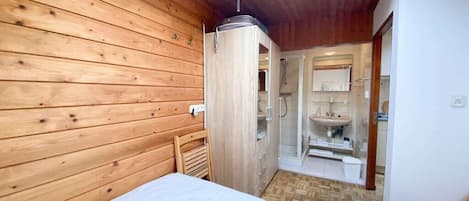 Una habitación con paneles de madera, una cama, una ducha y un lavabo.