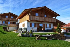 Eine zweistöckige Holzhütte mit Balkon, einer Terrasse mit Gartenmöbeln und einem gepflegten Rasen.
