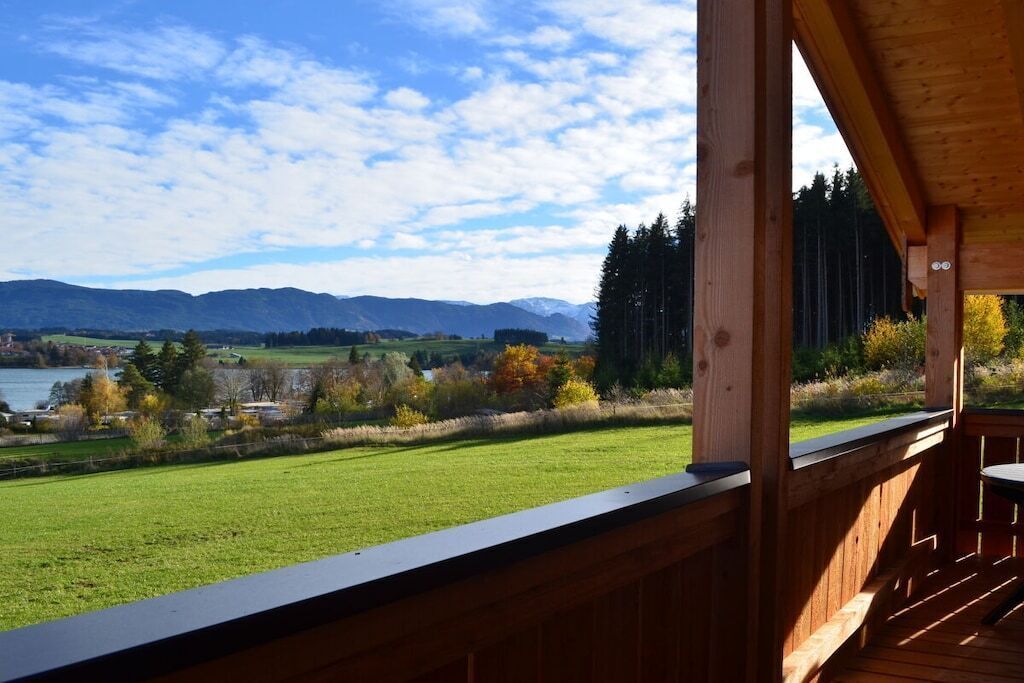 A wooden deck with a view of a green field, trees, and mountains in the distance.