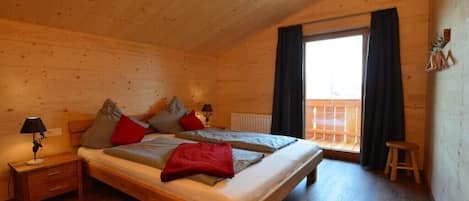 Een slaapkamer in een houten blokhut met een tweepersoonsbed, twee nachtkastjes, een nachtkastje, een raam met gordijnen en een houten kruk.