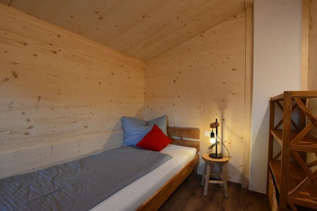 Ein Zimmer in einer Holzhütte mit einem Einzelbett, einem Nachttisch und einem kleinen Tisch.