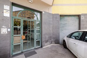Ein Gebäudeeingang mit Glastür, einem parkenden Auto und einer Garagentür.
