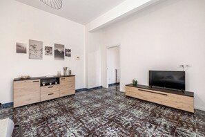 A modern living room with a large flat-screen TV, a wooden cabinet with drawers, and a patterned floor. - Mirea Domus - Salerno - Train Station/Bus/Ferry to Amalfi, 5 minutes away (Salerno)