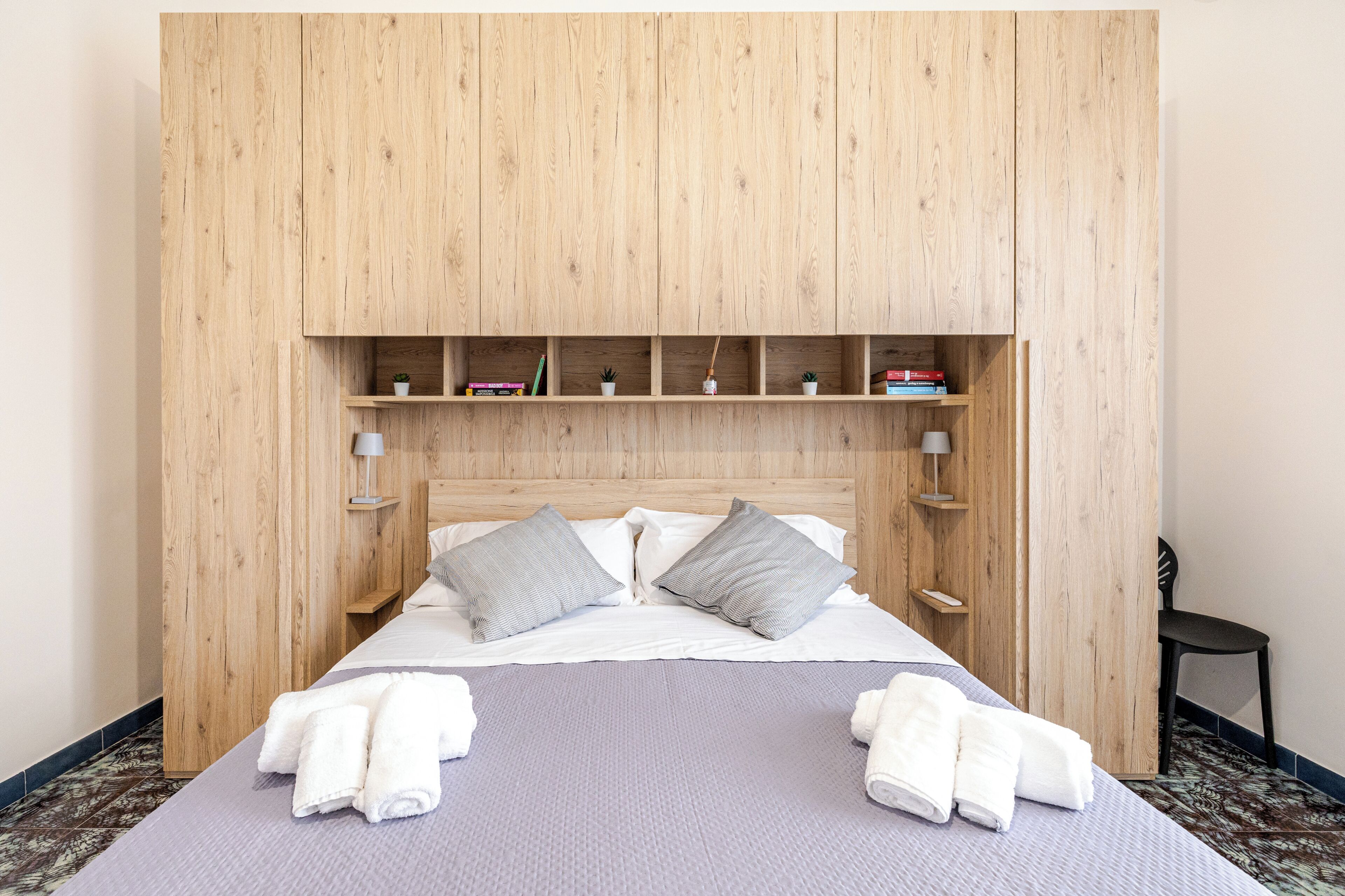 A bed with pillows, a bedside table, and a shelf above it.