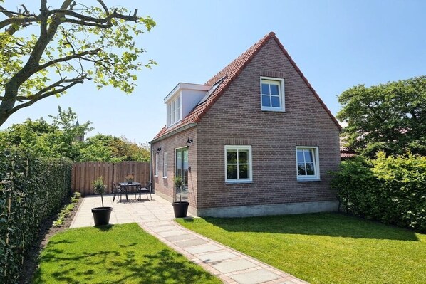 A two-story brick house with a sloped roof, a visible attic window, and a paved patio with outdoor furniture. - AK13 Holiday home near Domburg (Aagtekerke)