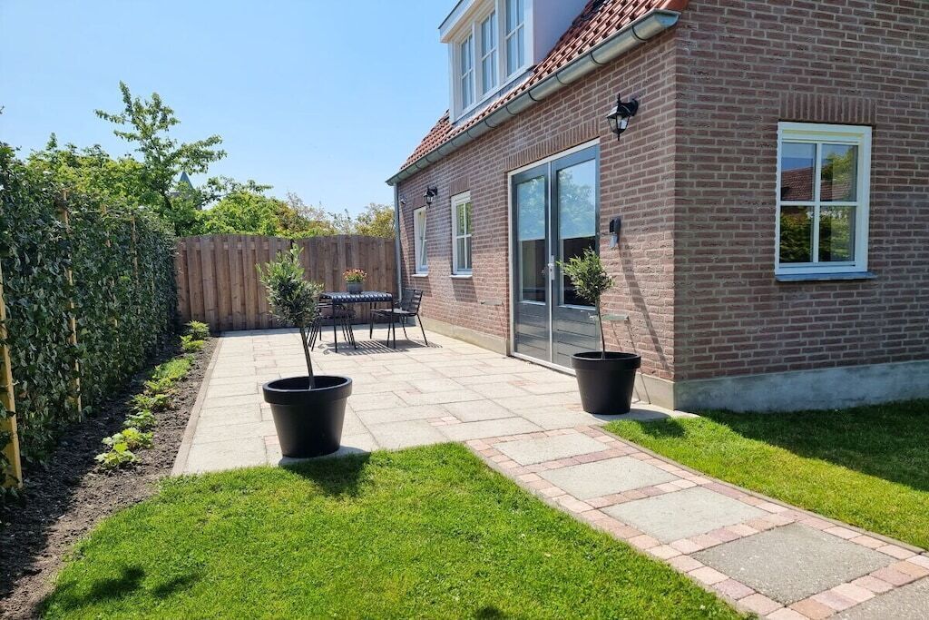 Ein Wohngarten mit Terrasse, Holzzaun und Backsteinhäuschen.