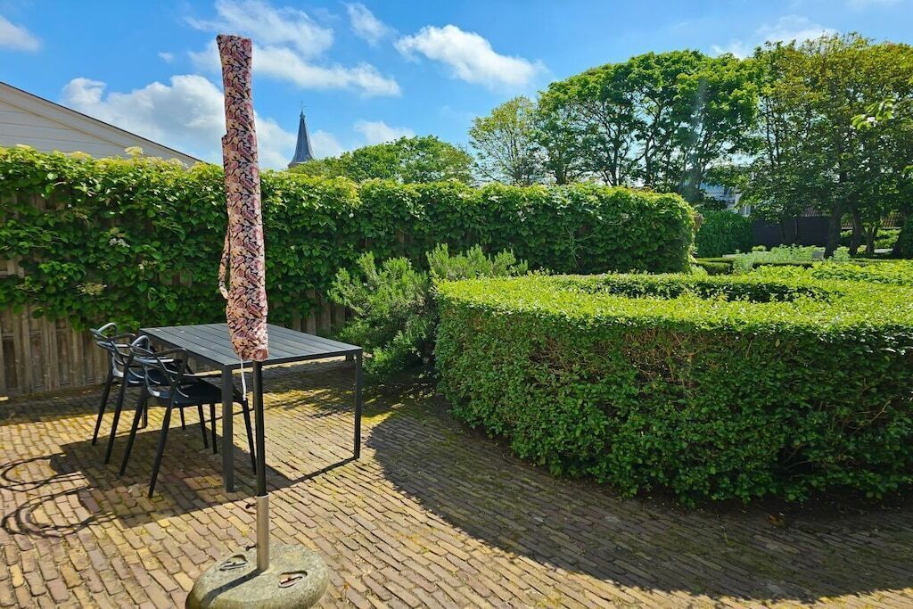 A brick patio with a table and chairs, surrounded by neatly trimmed hedges and trees.