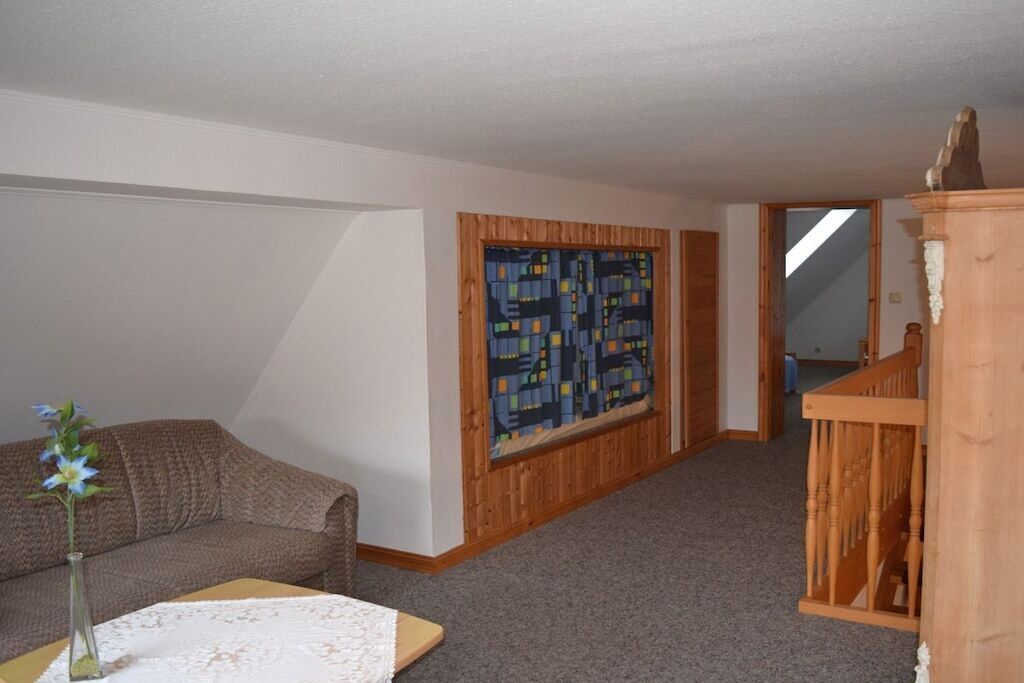 Ein Zimmer mit einem braunen Sofa, einem kleinen Tisch mit einer Vase, einem Holzschrank und einem großen, abstrakten Gemälde an der Wand.