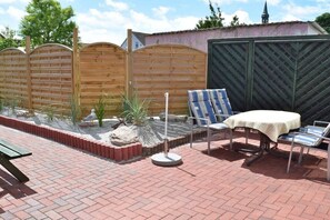A patio with a table and chairs, a wooden fence, and a brick border. - with sauna and fireplace (Tönning)