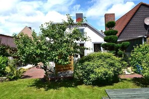 A residential area with a white house, a red-roofed building, and a well-maintained garden with a tree and bushes. - with sauna and fireplace (Tönning)