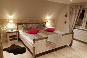 A bedroom with a wooden bed, two bedside tables with lamps, a stone wall, and a window with curtains. - Holiday apartment with 2 bedrooms (Braunlage)