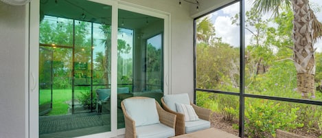 A covered outdoor seating area with wicker furniture and a glass door leading to a garden.