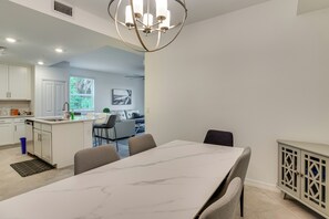 A modern kitchen with white cabinets, a dining area with a marble table, and a living room with a sofa and a TV. - Punta Gorda Resort Condo: Pool Access, Lanai (Punta Gorda)