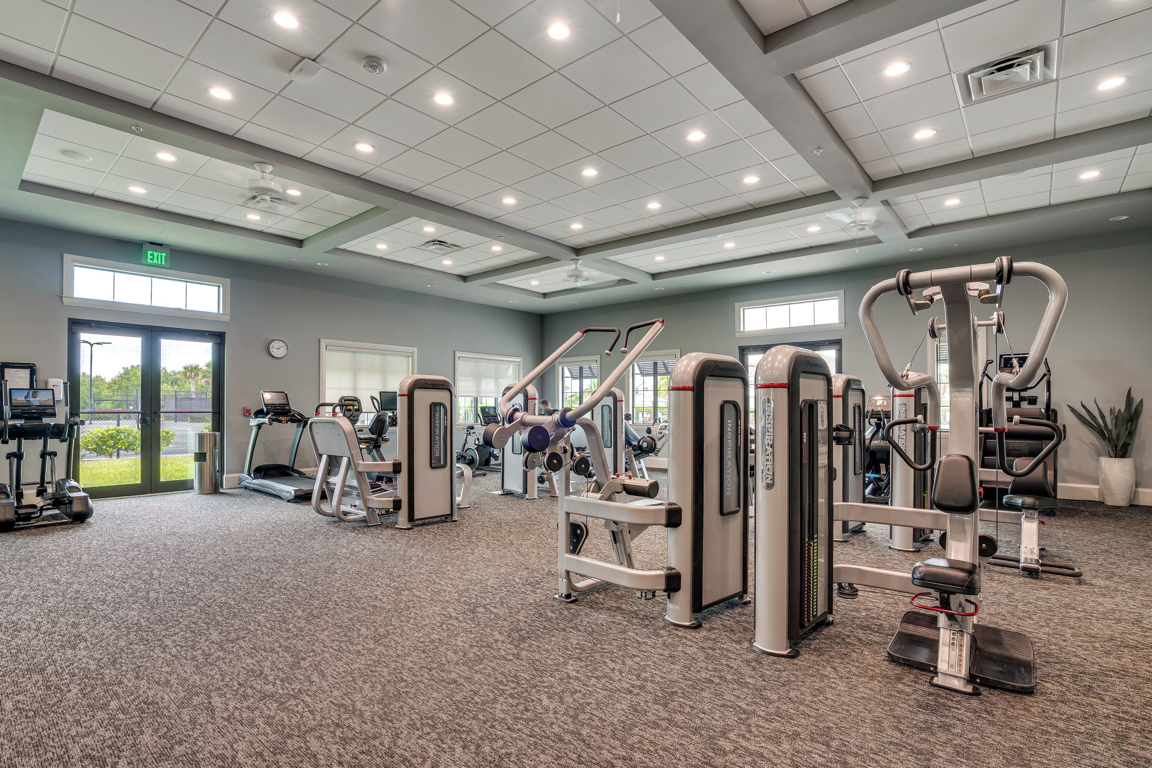A gym with various exercise equipment, a clock, and an exit sign.