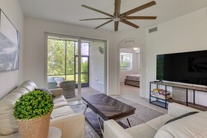 A modern living room with a ceiling fan, a flat-screen TV, and a large window providing a view of the outdoors. - Punta Gorda Resort Condo: Pool Access, Lanai (Punta Gorda)