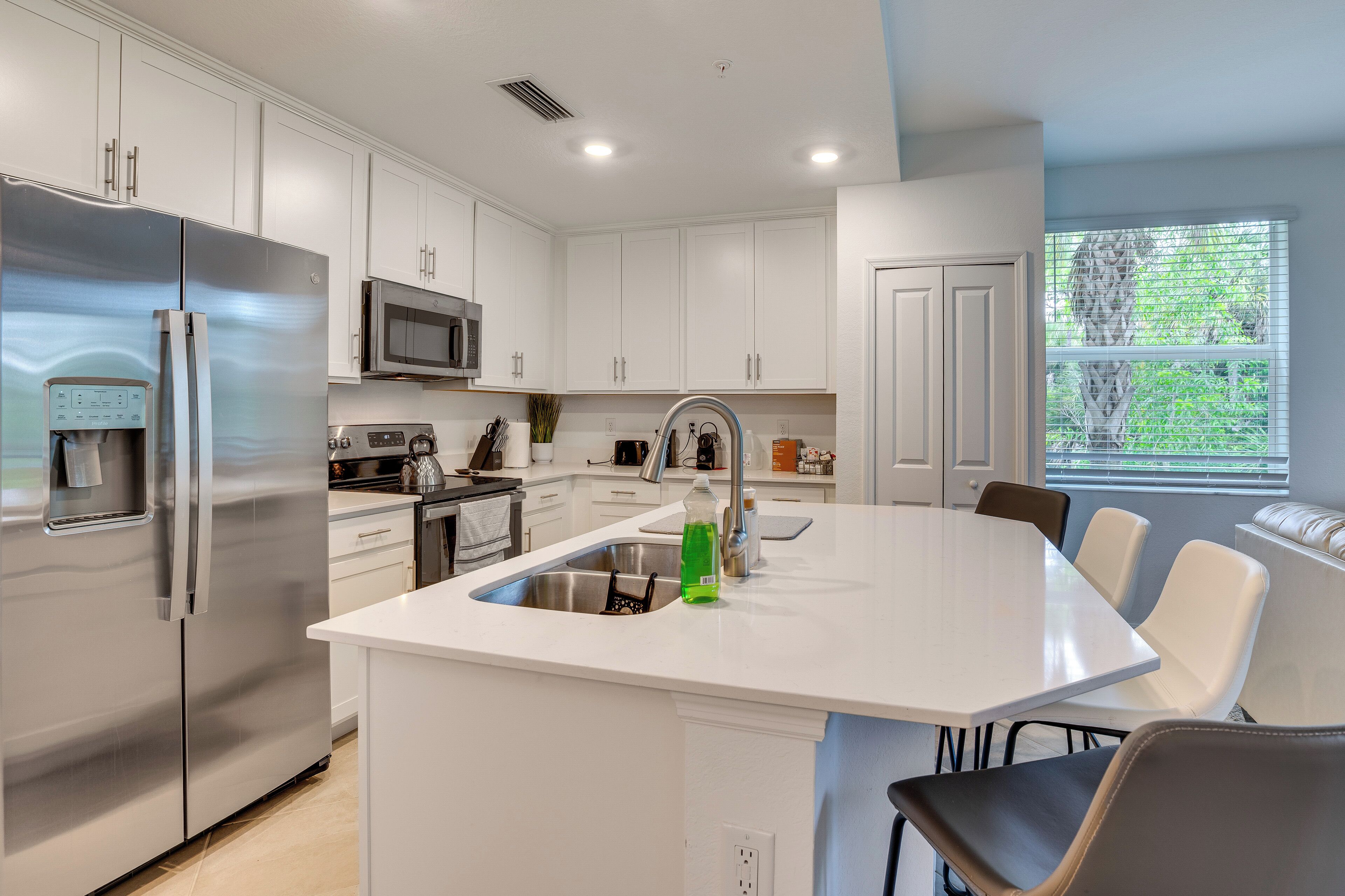 A modern kitchen with stainless steel appliances, a central island with seating, and a window with a view of greenery.