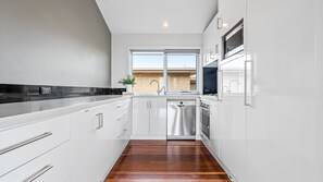 Una cocina moderna con muebles blancos, electrodomésticos de acero inoxidable y piso de madera.