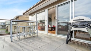 Een balkon met een barbecue, een glazen deur naar de binnenruimte en uitzicht op de omgeving.