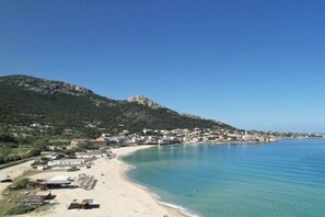 Eine Küstenstadt mit Strand, Gebäuden und einem Berg im Hintergrund.