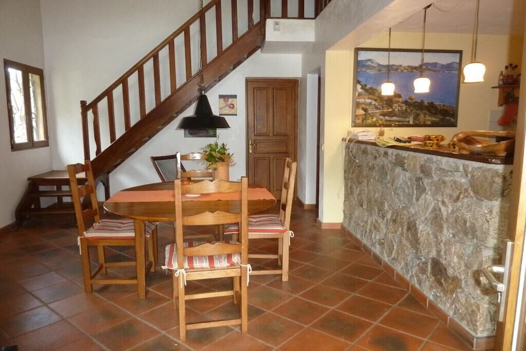 Un espace repas avec une table et des chaises en bois, un escalier et un comptoir de cuisine avec un pare-feu en pierre.