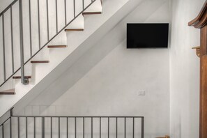 A staircase with wooden steps and metal railings, a flat-screen TV mounted on the wall, and a light switch.