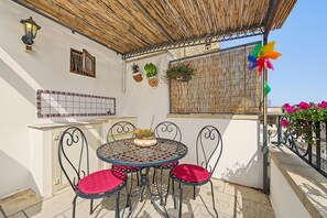 Un'area salotto esterna coperta con un tavolo rotondo e quattro sedie, una parete decorata con fioriere sospese e un soffitto in bambù.