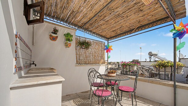 An outdoor patio with a table and chairs, a bamboo ceiling, potted plants, and a view of the cityscape. - 'La Casetta di Viola' charming and unique cottage just a few km from the sea! (Palmariggi)