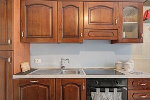 Una cocina con armarios de madera, un lavamanos de acero inoxidable y un lavavajillas negro.