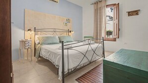 A bedroom with a bed, bedside table, lamp, air conditioning unit, and a window with curtains. - 'La Casetta di Viola' charming and unique cottage just a few km from the sea! (Palmariggi)