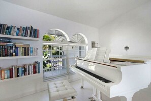 Ein Zimmer mit einem weißen Klavier, Bücherregalen und Blick durch eine Glastür.