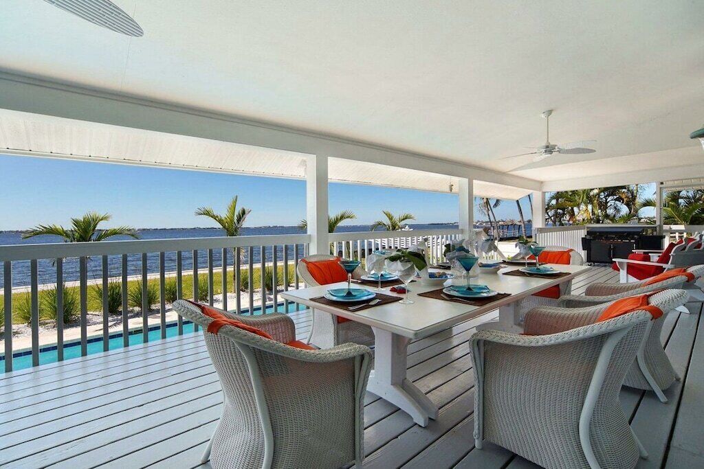 A covered outdoor dining area with a view of the sea, white furniture, and a pool.