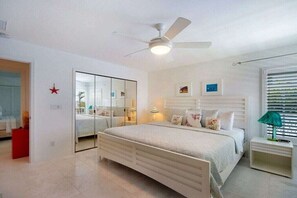 A bedroom with a bed, bedside tables, a ceiling fan, a mirror, and a window with blinds. - CCVS – Villa Southern Living (Cape Coral)